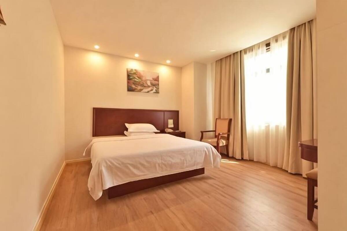 A hotel room with a large bed, a wooden headboard, a painting on the wall, a desk, and a chair.