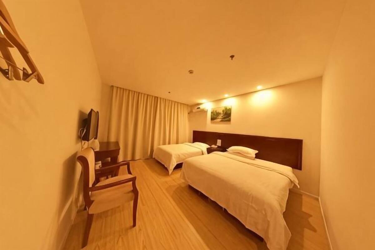 A hotel room with two beds, a desk, a chair, a TV, and a curtain.