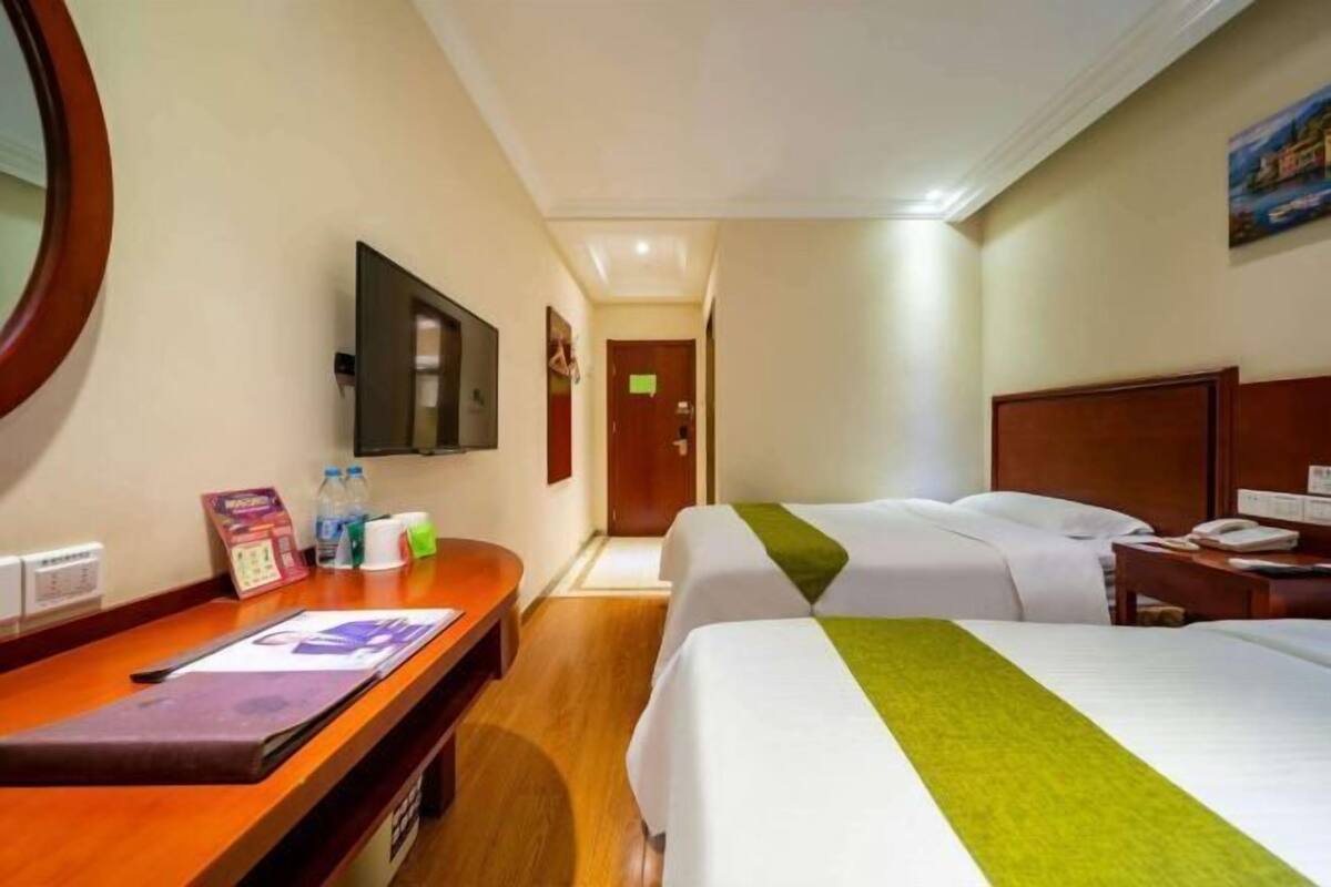 A hotel room with two beds, a desk, a TV, and a bathroom door.
