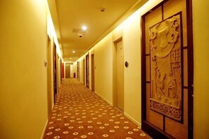 A hotel hallway with patterned carpet, doors, and a decorative wall.