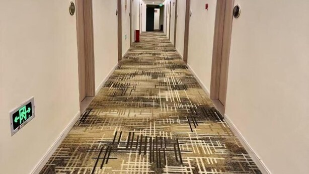 A hotel corridor with patterned carpet, doors on both sides, and emergency exit signs. - Pebble Motel (Shanghai Beidi Road) (Shanghai)