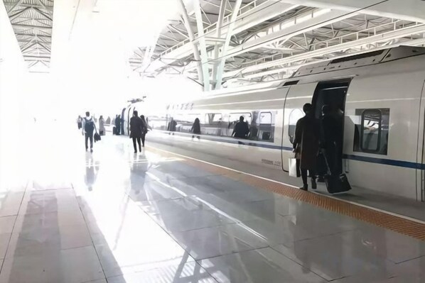 Andén de estación de tren con un tren, pasajeros y estructuras superiores.