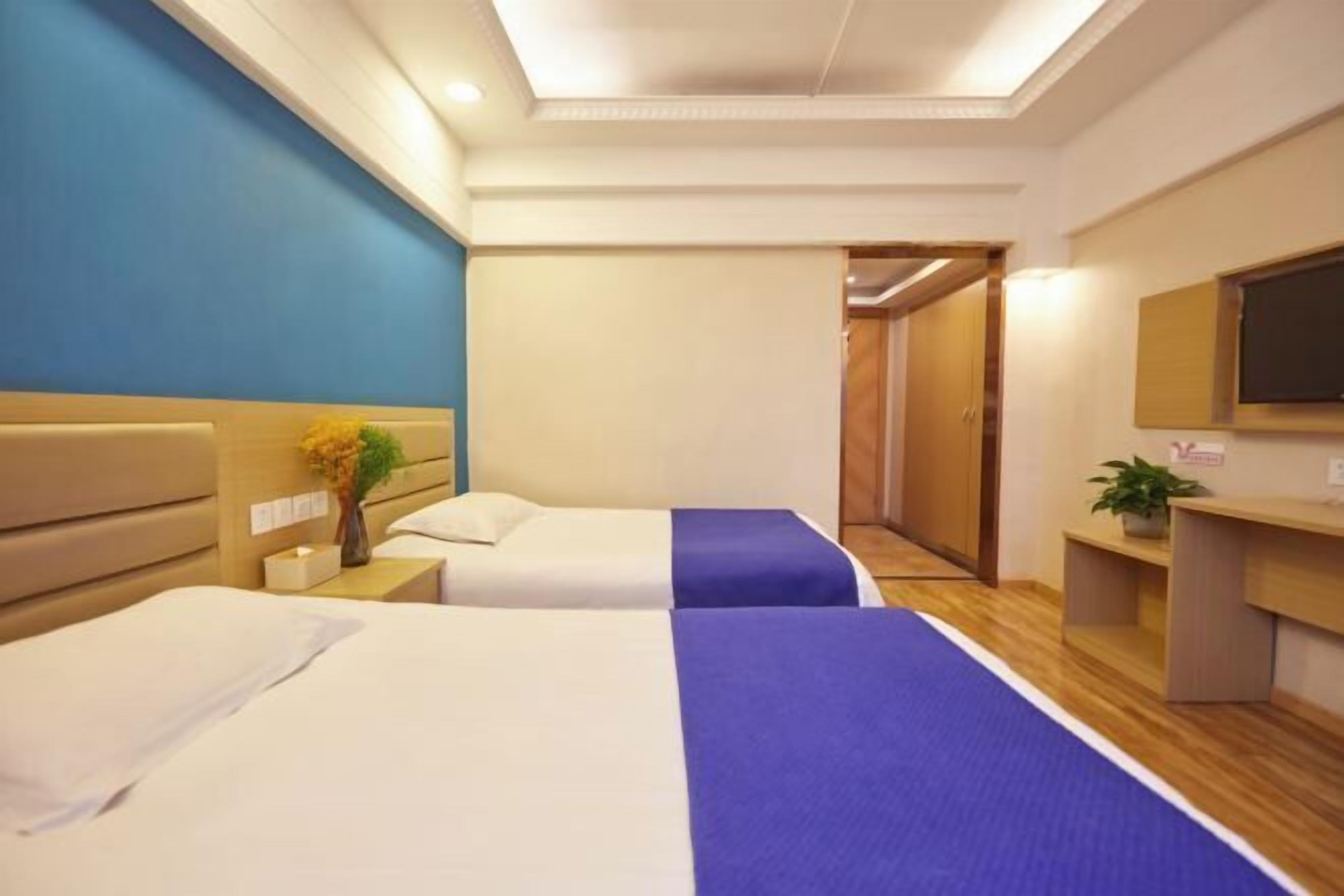 A hotel room with two beds, a desk, a chair, a TV, and a bathroom visible through an open door.