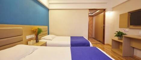 A hotel room with two beds, a desk, a chair, a TV, and a bathroom visible through an open door.