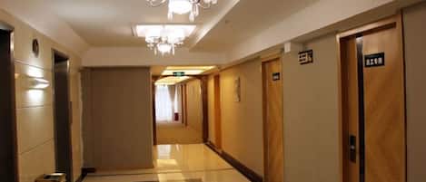 Un pasillo de hotel con candelabro, puertas con números de habitación y un cesto de basura.