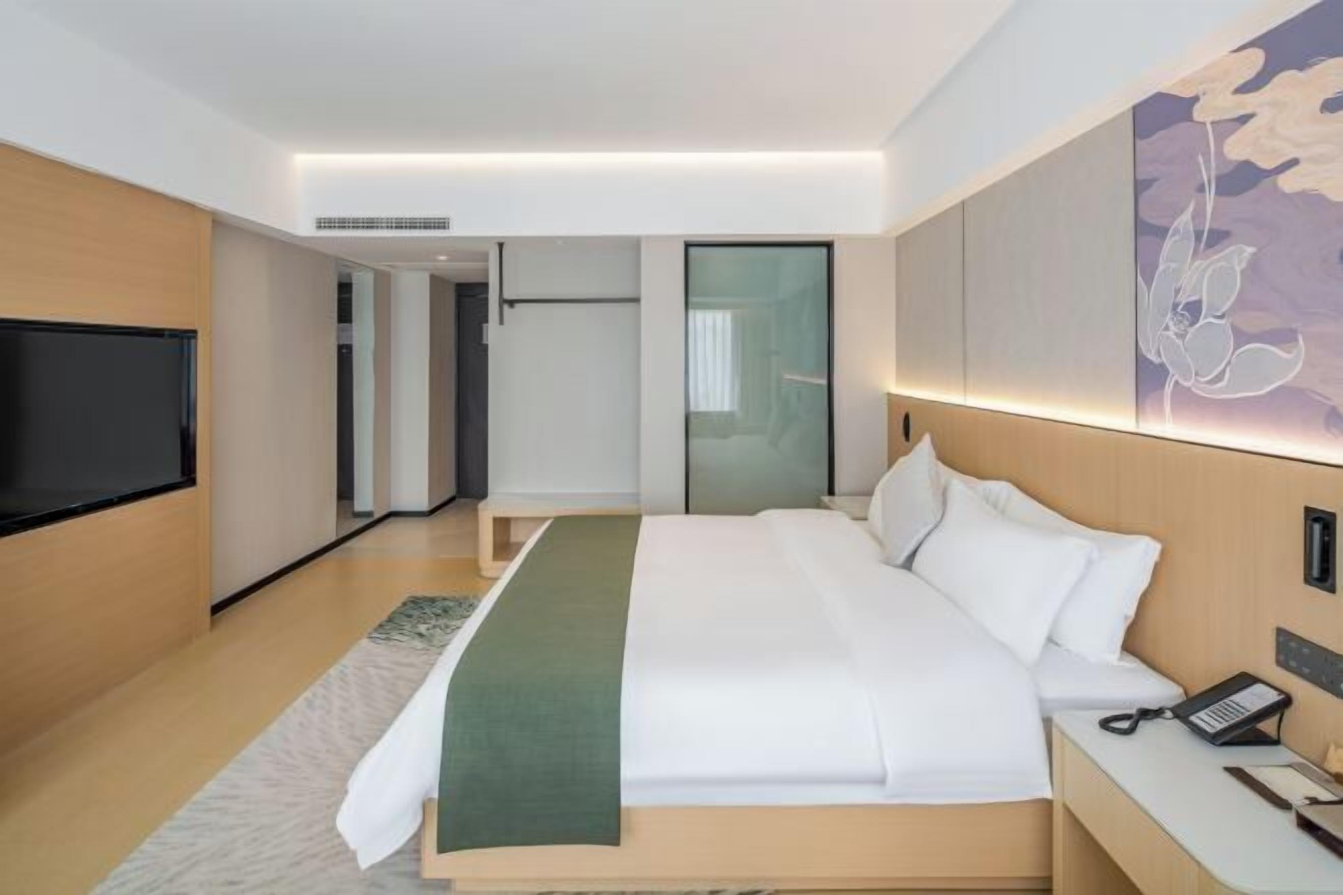 A modern hotel room with a large bed, a bedside table with a phone, a flat-screen TV, and a wall-mounted artwork.