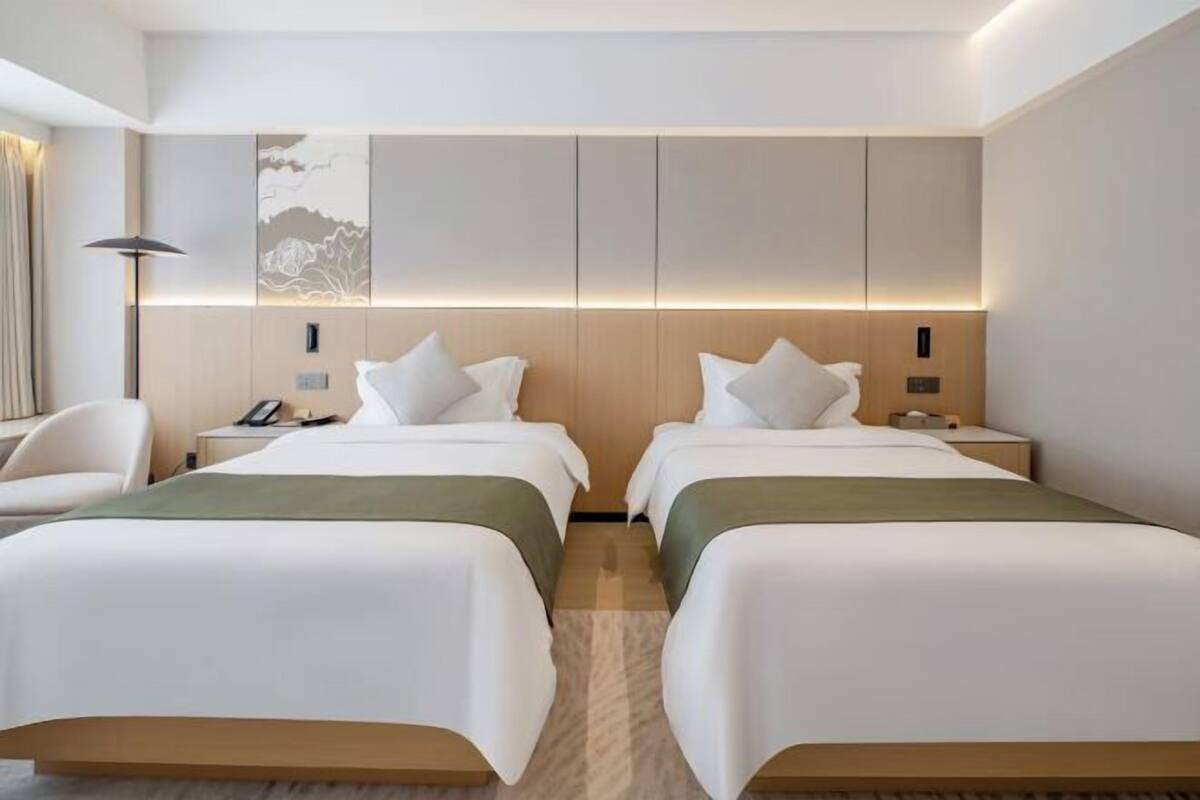A hotel room with two beds, a desk, a chair, and a lamp.