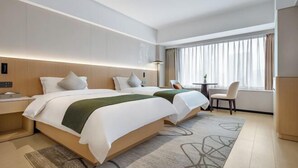 Ein Hotelzimmer mit zwei Betten, einem Schreibtisch, einem Stuhl und einem großen Fenster mit Vorhängen.