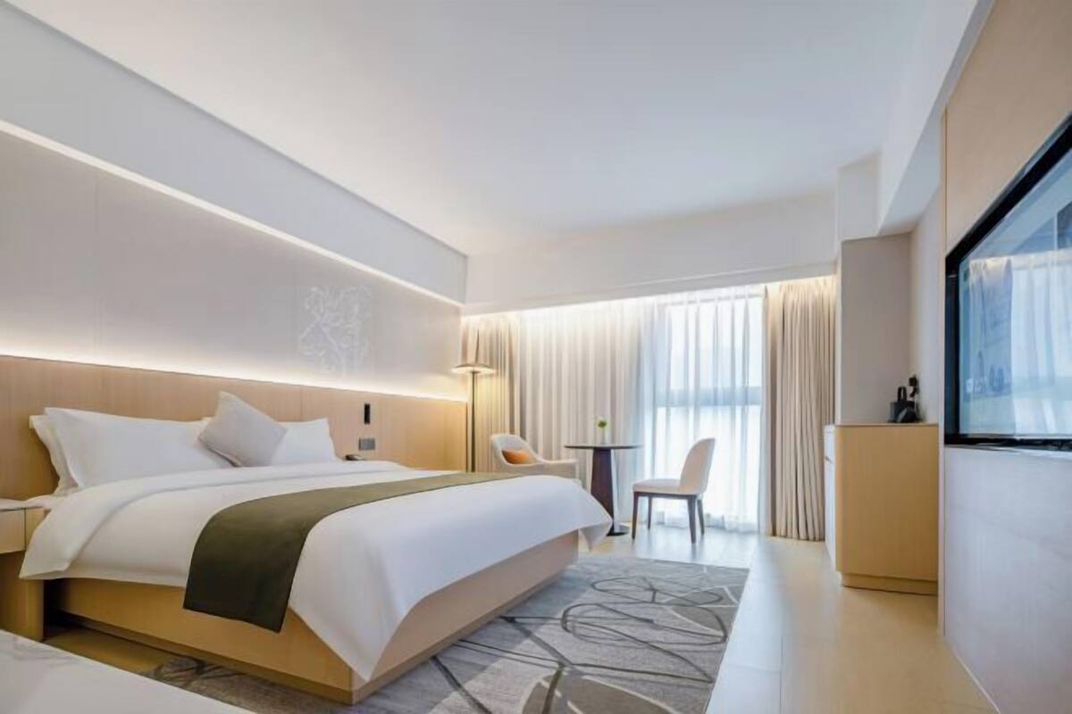 A modern hotel room with a large bed, bedside tables, a desk, and a view of the outdoors.