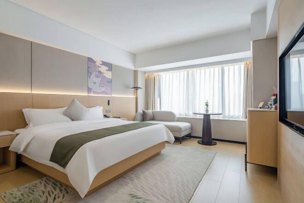 A modern hotel room with a large bed, a seating area, a small table, and a TV.