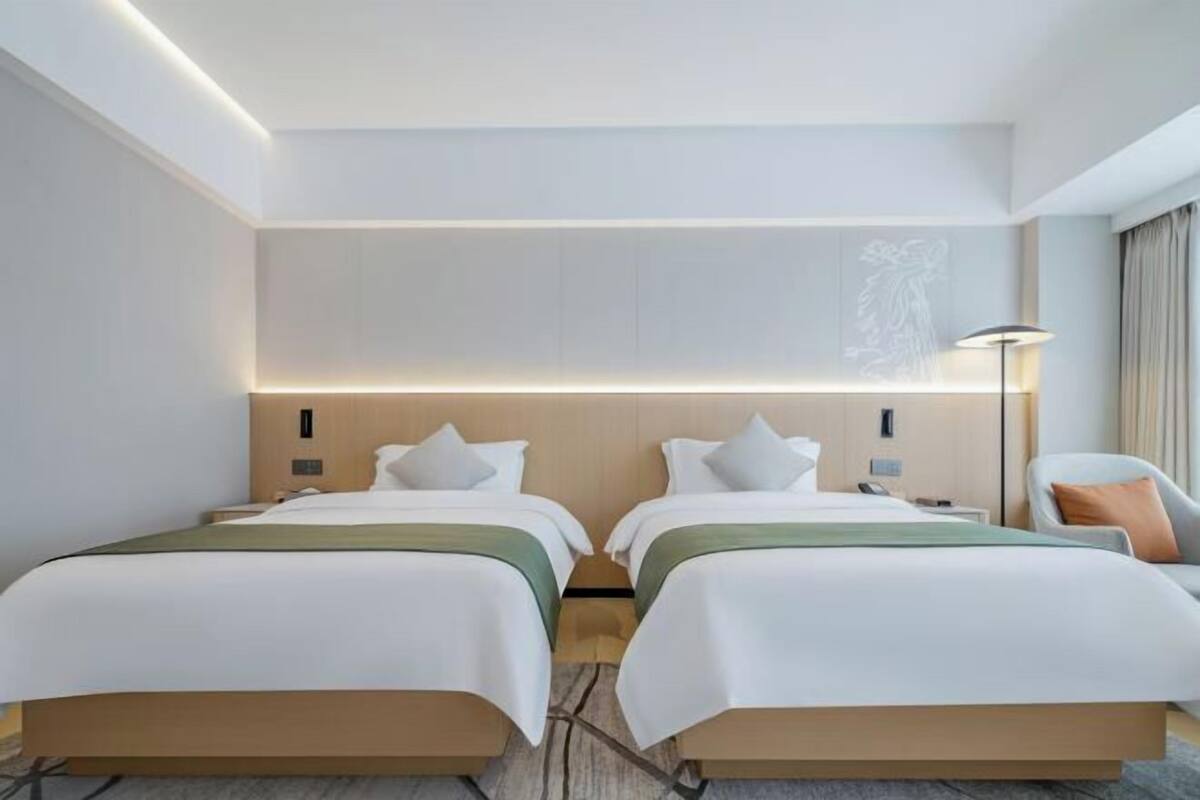 A hotel room with two beds, a desk, a chair, and a lamp.