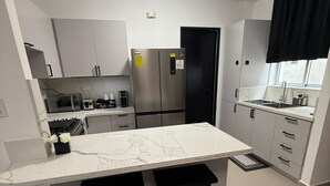Une cuisine moderne avec un plan de travail en marbre blanc, deux tabourets noirs, des appareils électroménagers en acier inoxydable et une porte noire.