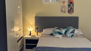 Un dormitorio con cama, mesita de noche, lámpara, aire acondicionado instalado en la pared y un armario.