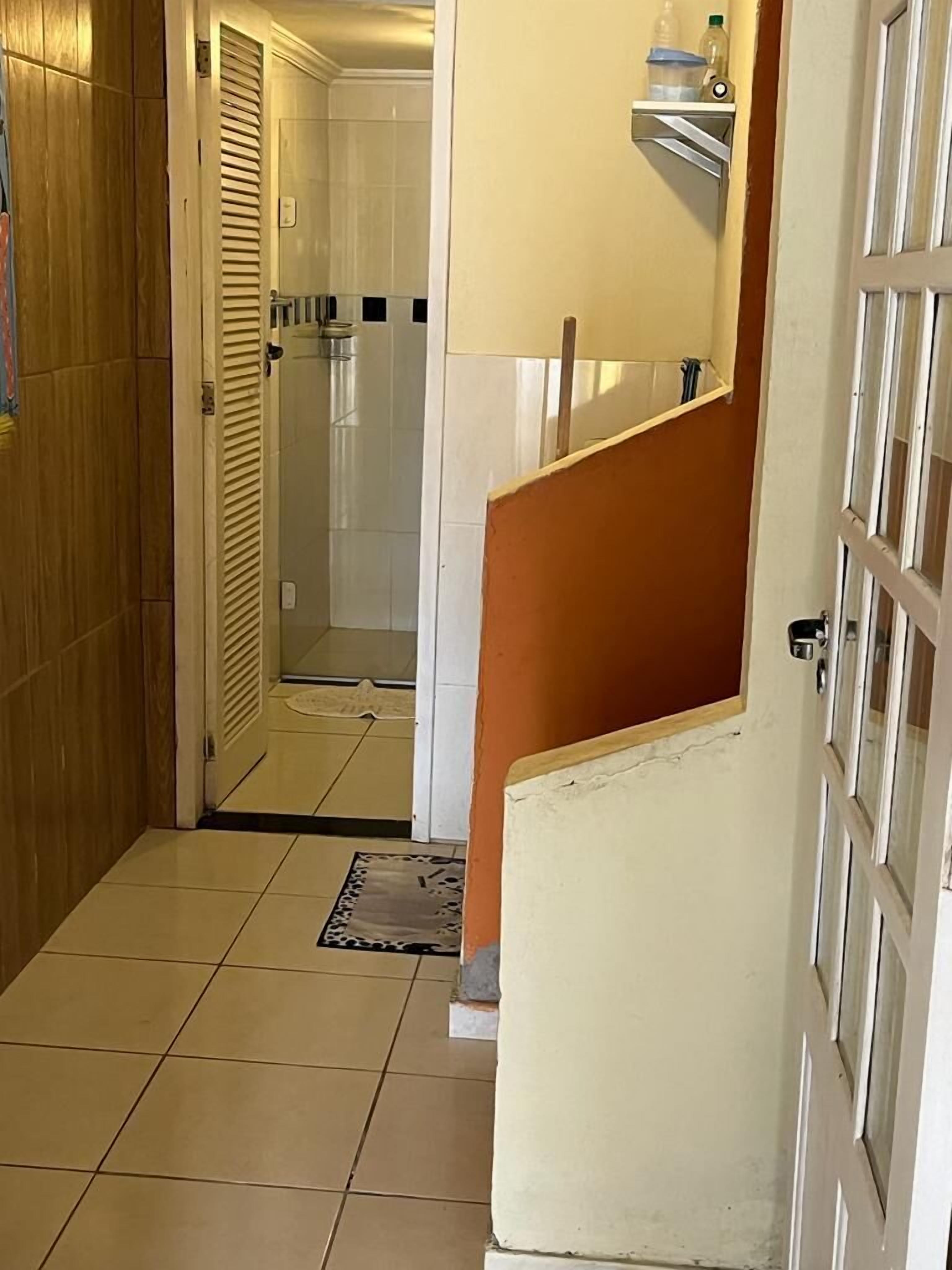 Un couloir avec une porte en bois, un sol carrelé de carreaux blancs et une salle de bain visible à travers une porte en verre.