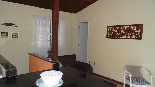 A dining area with a black table, white chairs, and a decorative wall piece. - Ogiva 3 quartos com cama de casal (Cabo Frio)