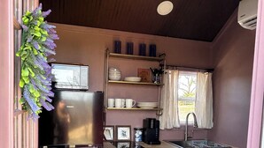 Una cocina pequeña equipada con refrigerador, estantes, pileta y ventana.