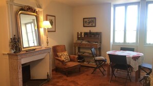 A cozy room with a fireplace, a comfortable armchair, a small table with chairs, and a bookshelf. - Le Pré Blanc - CHANGE - Gîte (CHANGE)
