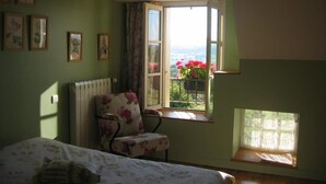 A bedroom with a bed, a chair, a window with a view of flowers, and a radiator. - Le Pré Blanc - CHANGE - Gîte (CHANGE)