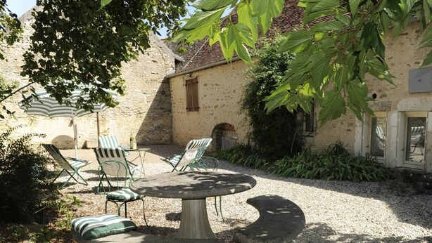 A stone table with chairs in a courtyard, surrounded by greenery and a building with a stone facade. - Le Pré Blanc - CHANGE - Gîte (CHANGE)