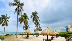 A beachside area with thatched umbrellas, wooden chairs, and palm trees. - VIP Apartment - With Sea and Beach View (Santa Marta)
