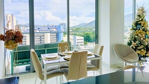 A dining area with a table set for four, large windows offering a cityscape view, and a Christmas tree in the corner. - VIP Apartment - With Sea and Beach View (Santa Marta)