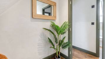 Ein Flur mit Holzboden, einem Blumentopf, einem Spiegel an der Wand und einer Tür zu einem anderen Raum.
