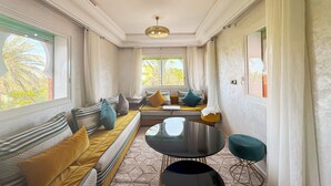 A room with a long sofa, a small round table, and a window with curtains. - Luxurious Duplex in a Peaceful Resort (Marrakech)