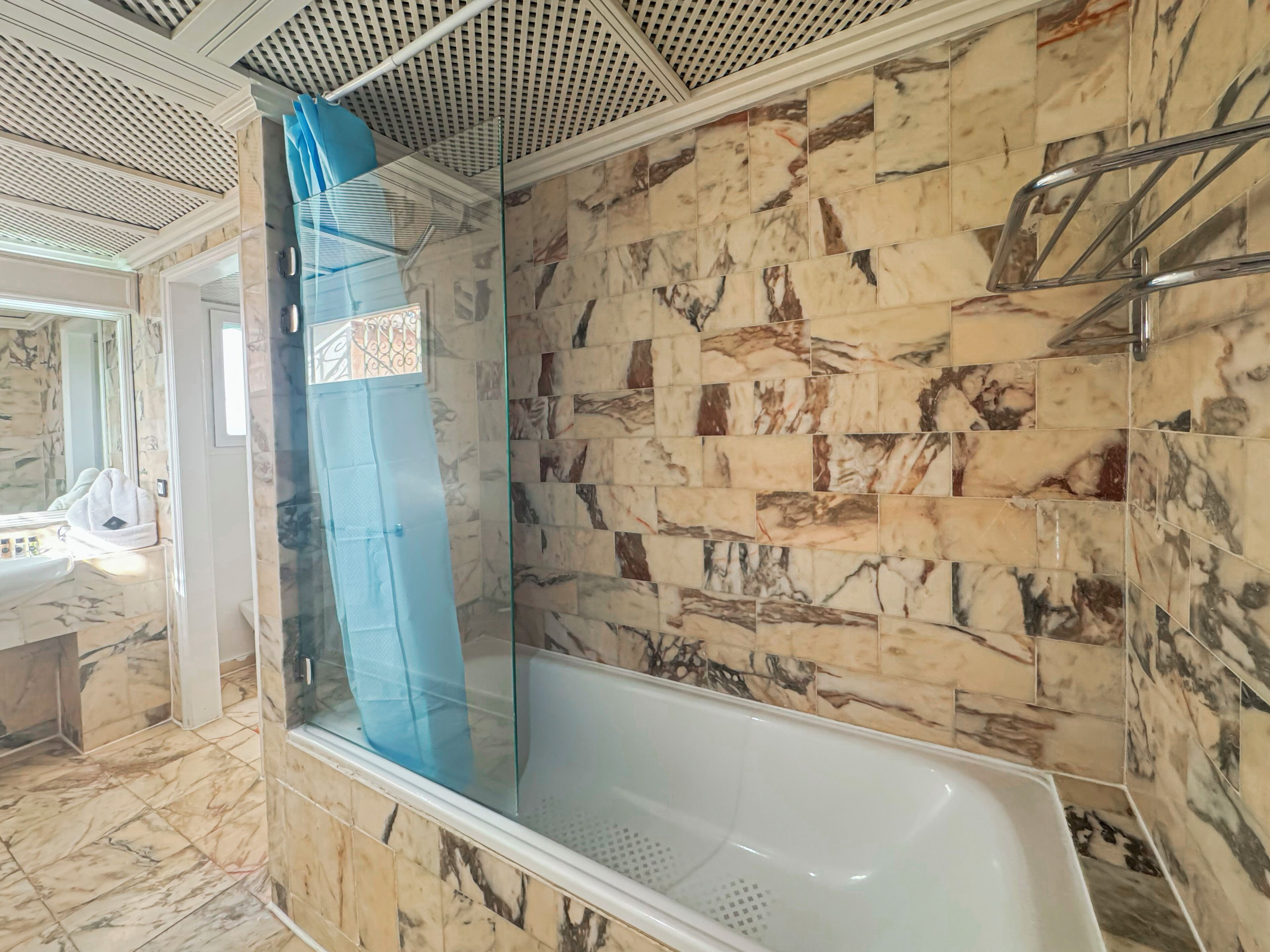 A bathroom with a marble-tiled shower enclosure, a glass shower door, and a white bathtub.