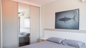 Un dormitorio con cama, mesita de noche, aire acondicionado instalado en la pared y un cuadro enmarcado de una ballena.