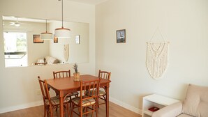 Un comedor con mesa y sillas de madera, una mesita auxiliar blanca y un colgador de macramé en la pared.