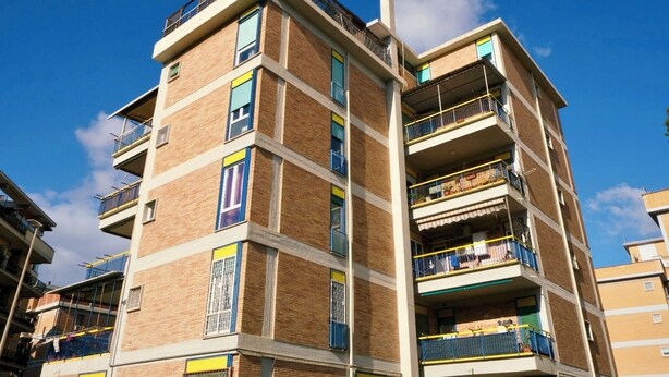 A multi-story residential building with balconies, brick facade, and a clear blue sky.