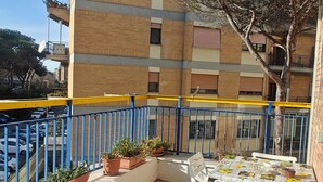 A covered outdoor seating area with a table and chairs, potted plants, and a view of a building with balconies.