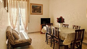 A dining area with a table set for four, a sofa, a television, and a painting on the wall.
