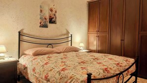 A bedroom with a bed, nightstand, wall art, and wooden wardrobe.