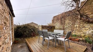 Un patio con una mesa y sillas, un muro de piedra y una terraza de madera.