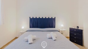 A neatly made bed with two rolled towels, a dark headboard, and two bedside lamps.