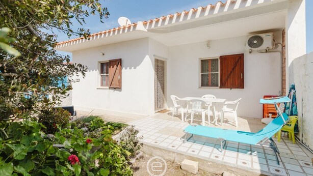 A white building with a tiled patio, a pool, and outdoor furniture.