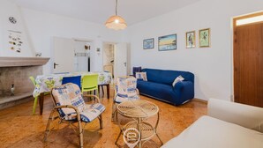 A living room with a blue sofa, wicker chairs, a dining table with a floral tablecloth, and a hanging lamp.