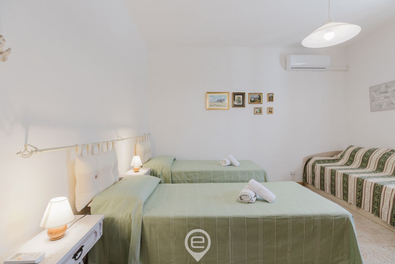 Une chambre d’hôtel avec deux lits simples, une table de chevet avec une lampe, un climatiseur fixé au mur et des tableaux encadrés accrochés au mur.