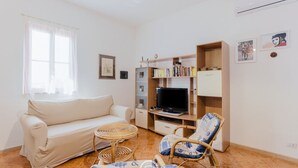 A living room with a sofa, a television, a bookshelf, and a wicker chair.