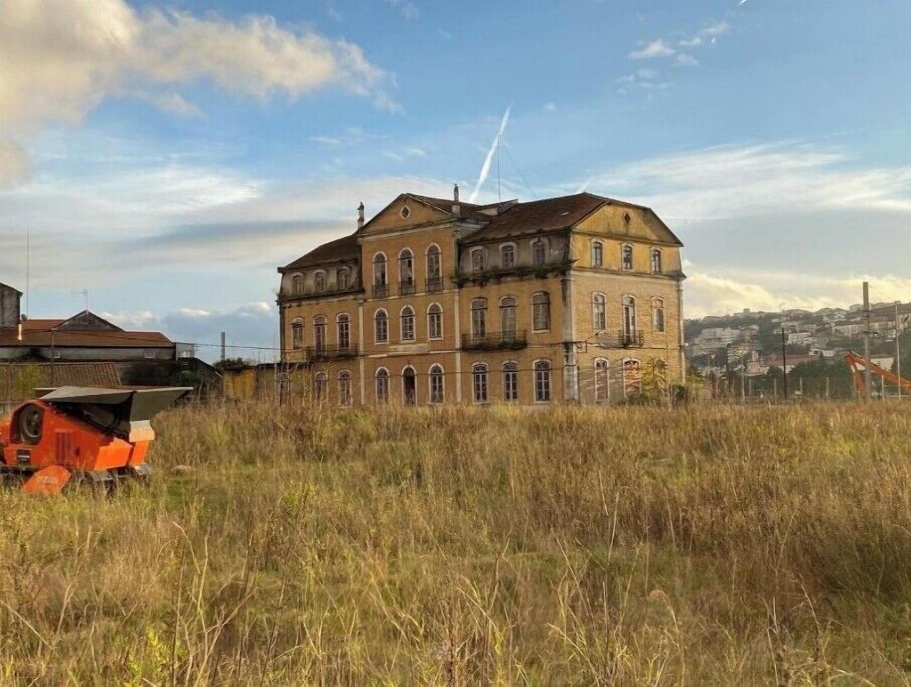 A large, historic building with multiple windows and a prominent central tower, surrounded by tall grass and a clear sky.
