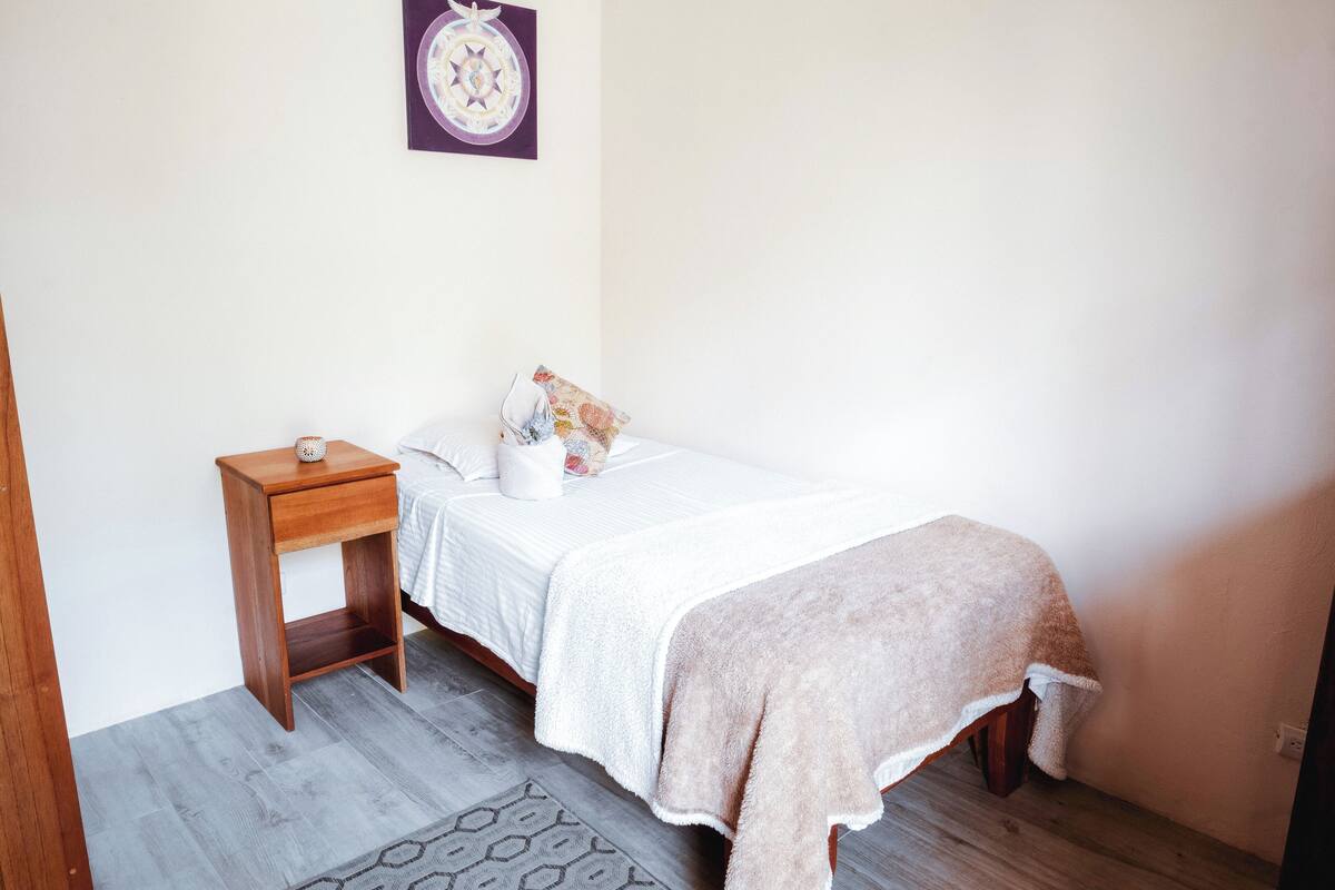 A bedroom with a bed, a bedside table, a wall-mounted decorative plate, and a patterned rug.