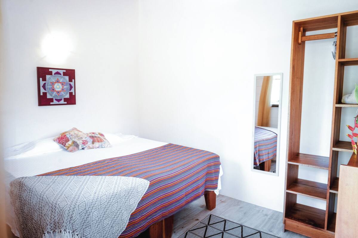 A bedroom with a bed, a bedside table, a mirror, and a wardrobe.