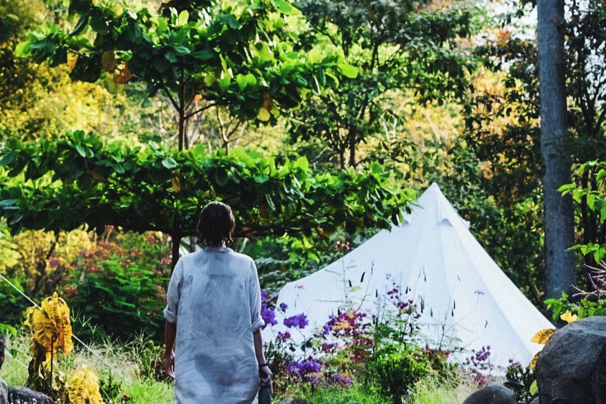 A person walking on a gravel path towards a white tent in a natural setting with trees and greenery.