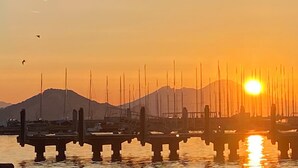 Une vue sur un coucher de soleil au-dessus d’une marina, avec des bateaux amarrés et un pont au premier plan.