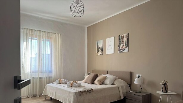 A bedroom with a bed, bedside tables, a nightstand, a lamp, and artwork on the wall.
