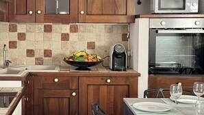 A kitchen with wooden cabinets, a microwave, an oven, a coffee maker, and a dining table set with plates and glasses.