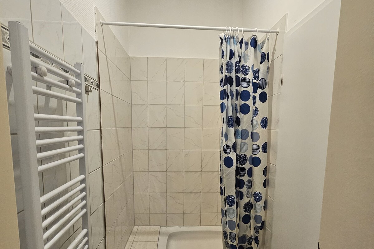 Um espaço de chuveiro pequeno e fechado com um cortina branca decorada com um padrão de bolinhas azuis e brancas.