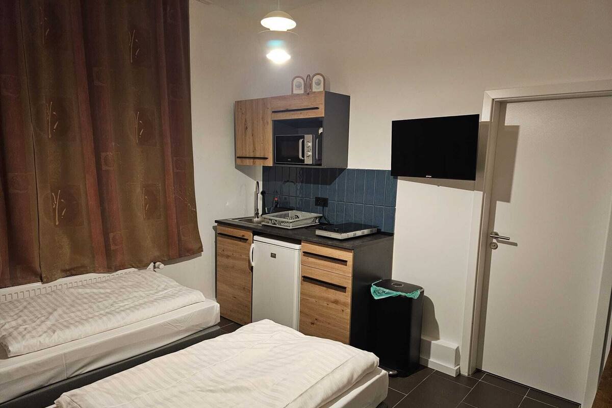 Habitació senzilla amb llit, petita cuina, televisió i una porta.