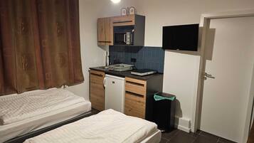 A compact room with a bed, a small kitchenette, a TV, and a door.
